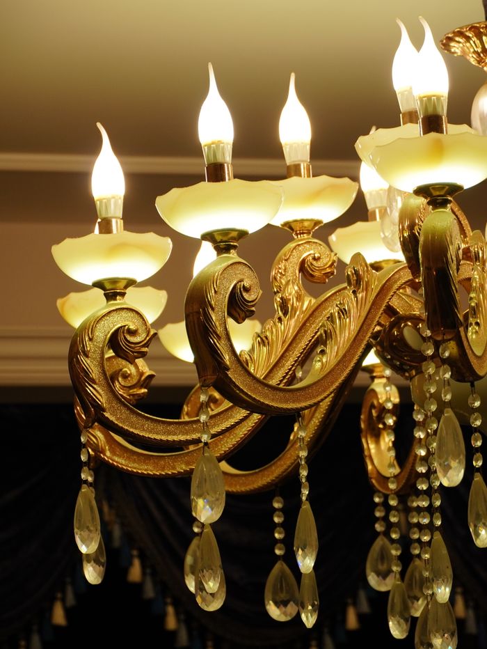 Services Luxurious golden chandelier featuring intricate designs and ornate crystal pendants, glowing warmly indoors.
