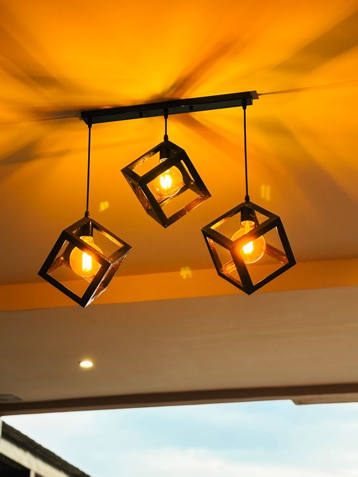 Services Artistic display of modern pendant lights with an industrial design against a vibrant yellow ceiling.